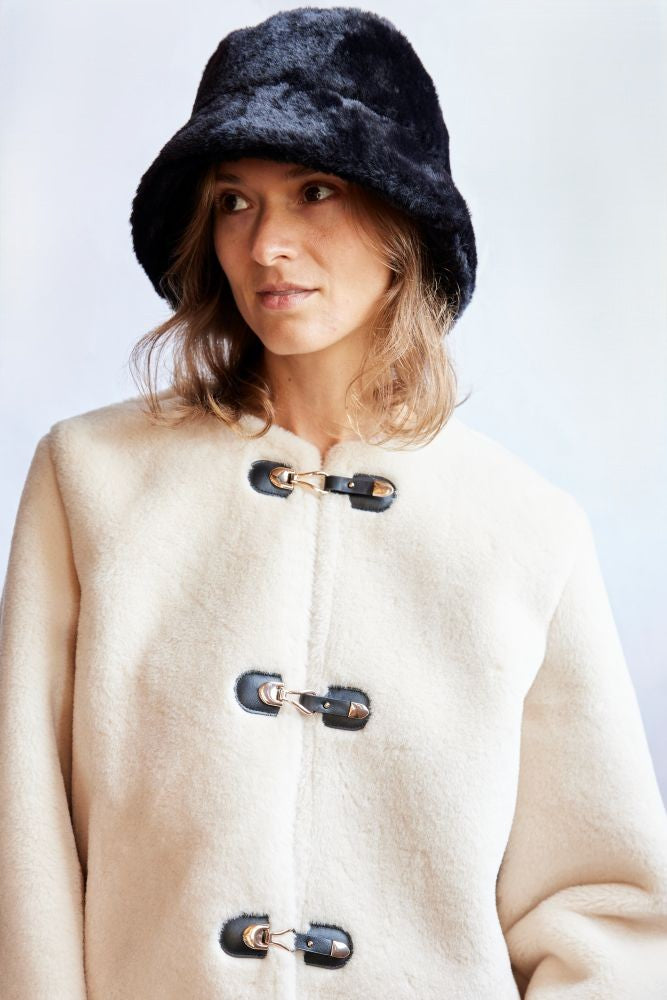 Woman wearing a beige coat with black buttons and a black faux fur hat on a white background