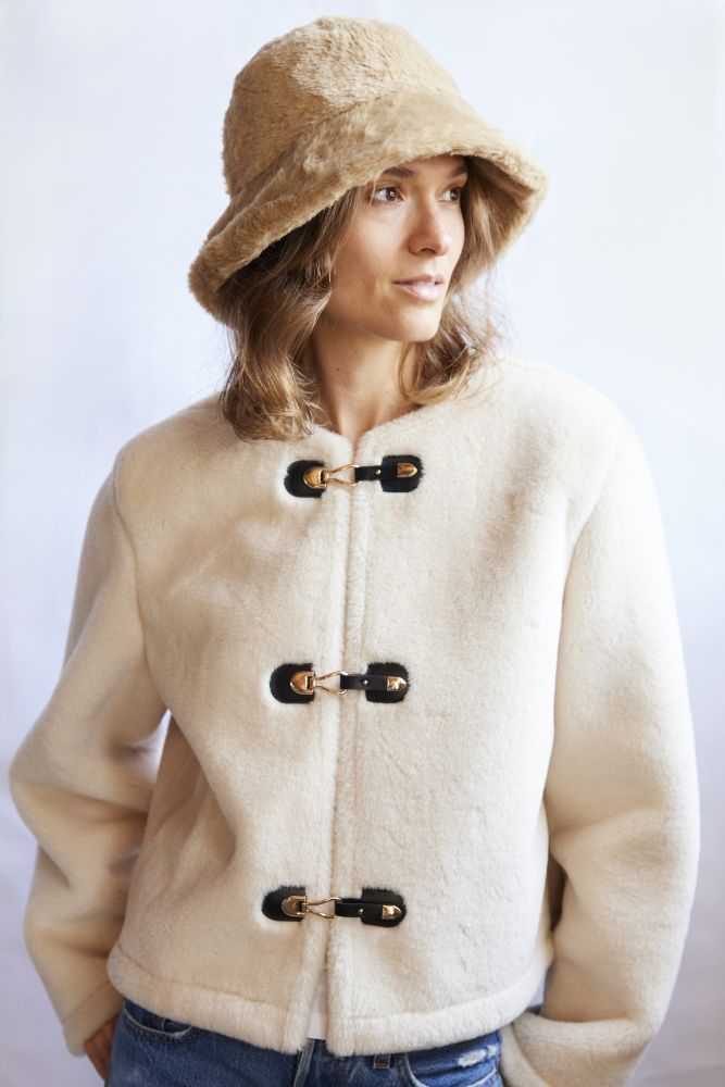 Woman wearing a beige coat with black buttons and a matching faux fur hat on a white background