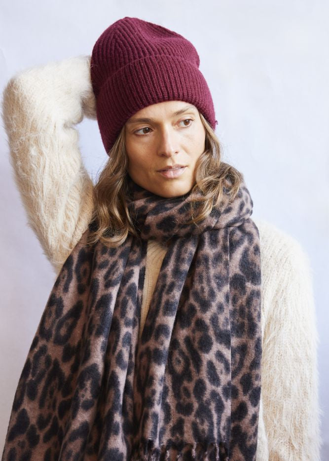 Woman wearing a leopard print scarf and maroon beanie against a white background