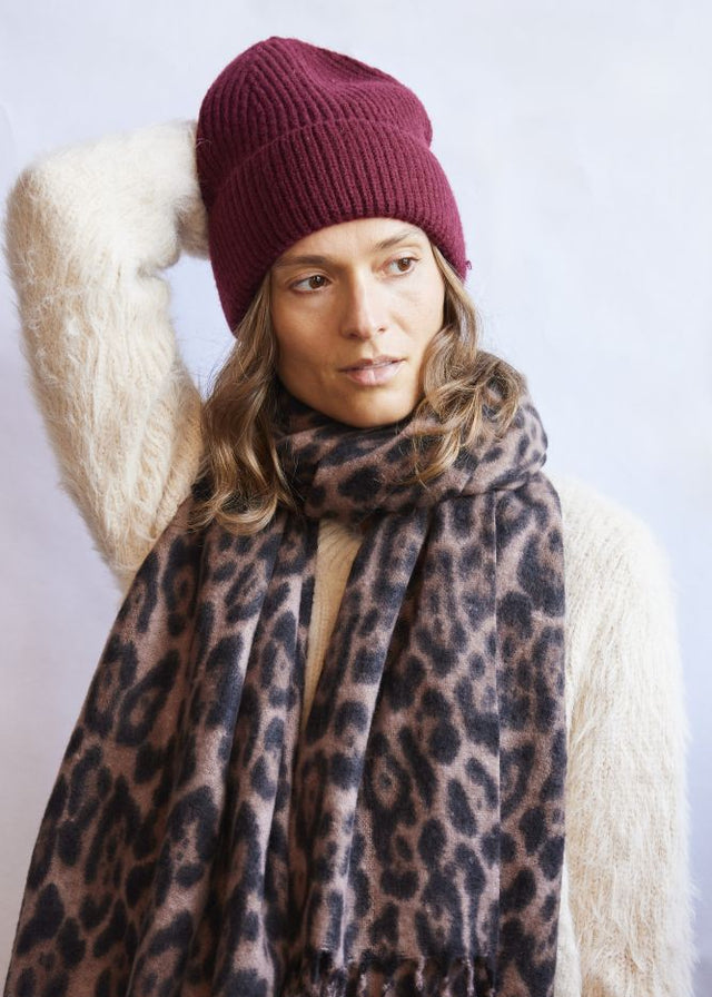 Woman wearing a leopard print scarf and maroon beanie against a white background