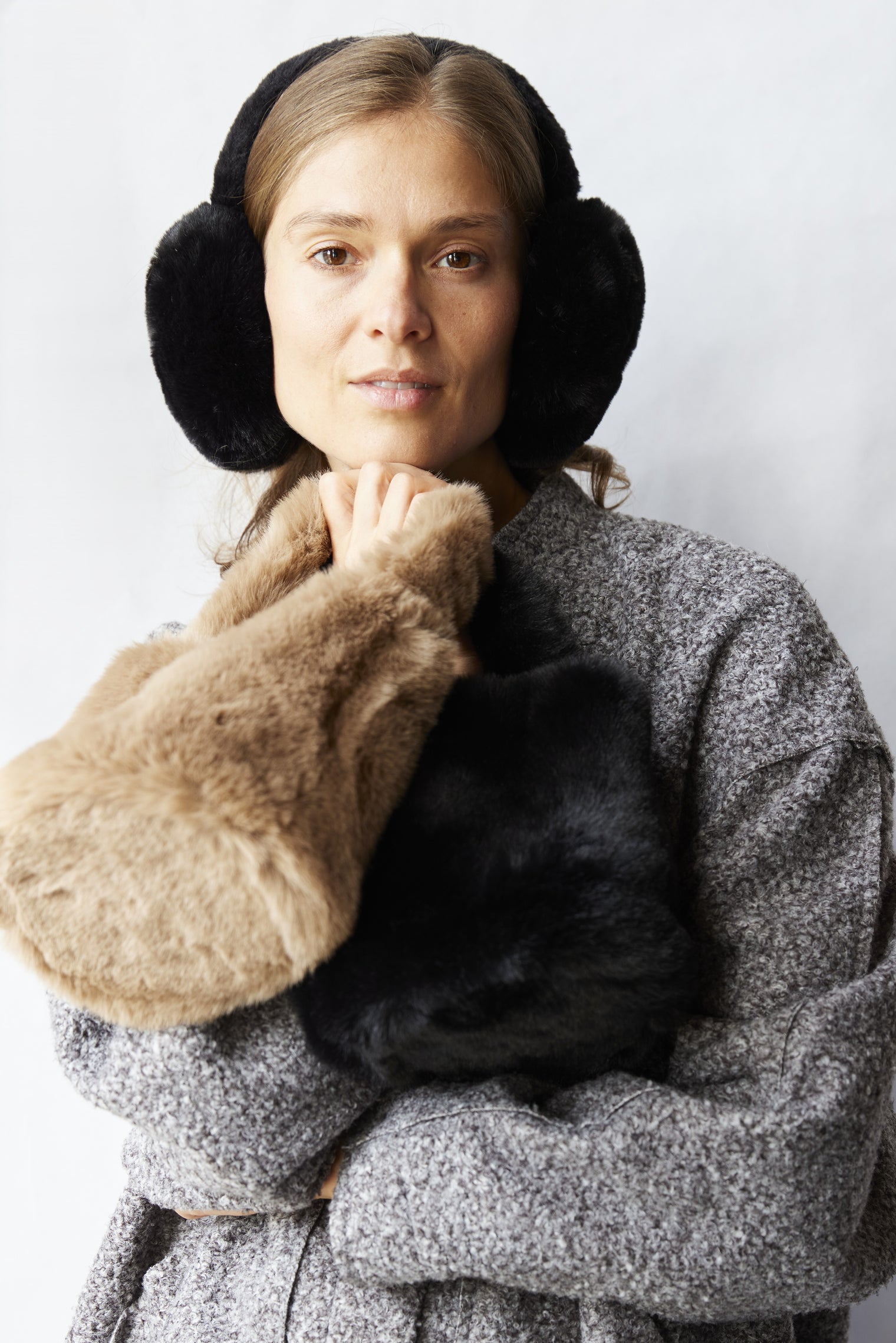 Woman wearing a gray coat and black earmuffs with a white background