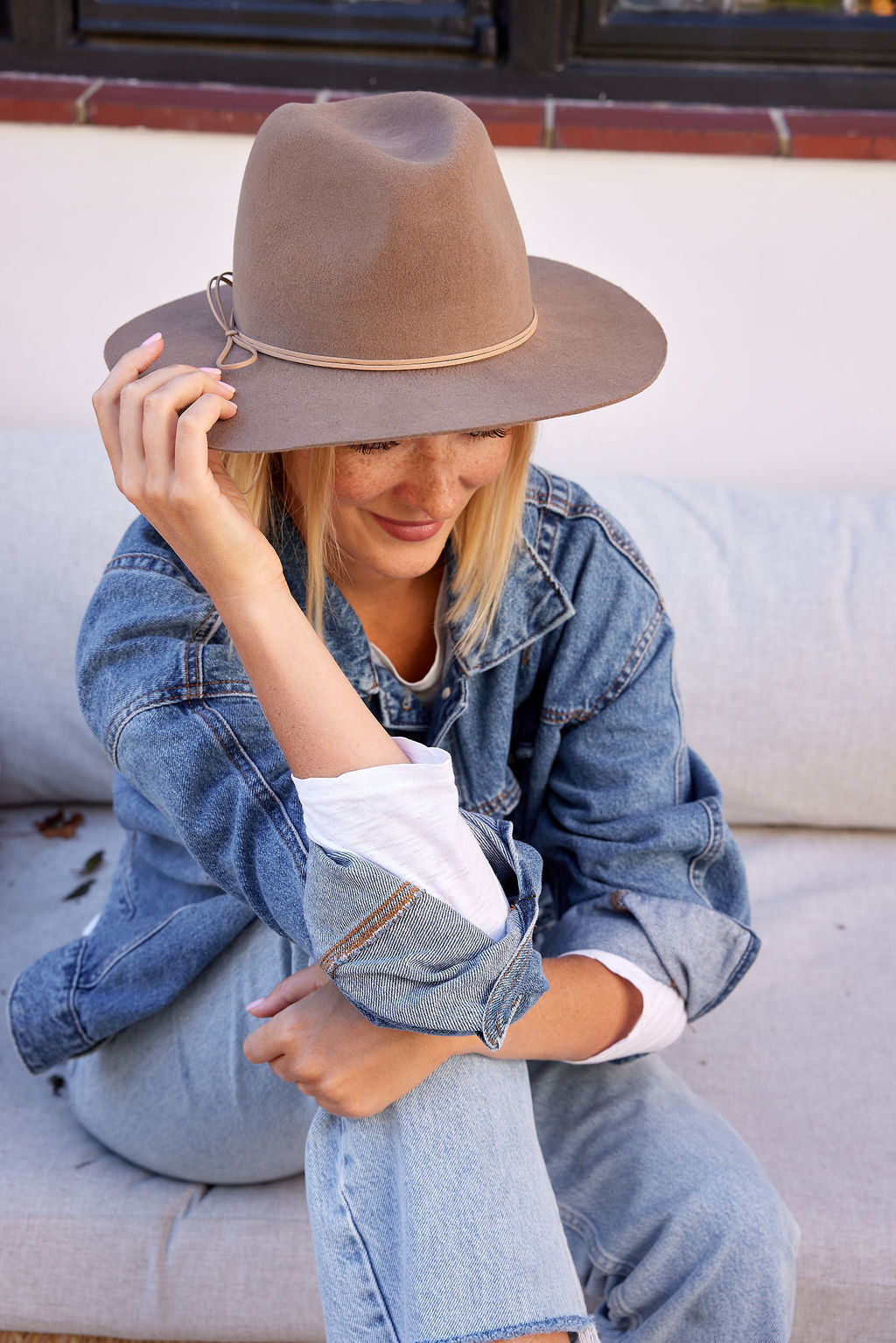 Woman wearing a brown hat and denim jacket sitting on a couch.