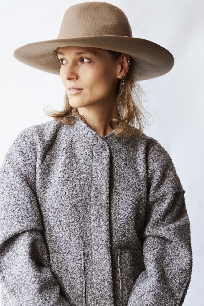 Woman wearing a wide-brimmed hat and a textured coat against a plain background