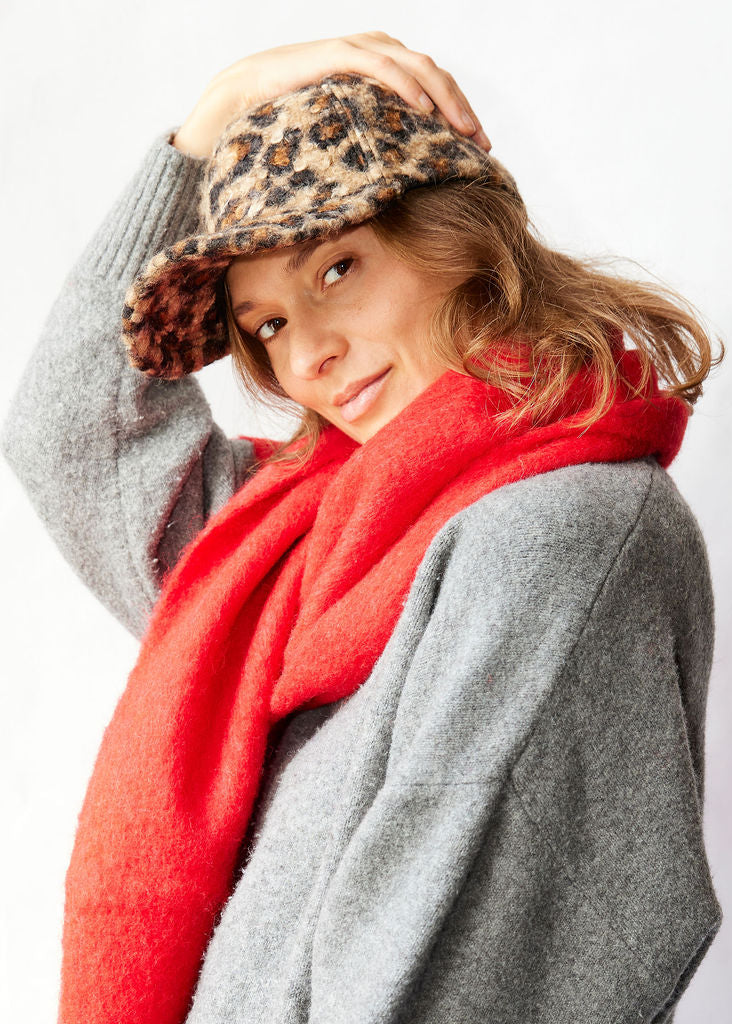Woman wearing a leopard print hat, red scarf, and gray coat on a white background