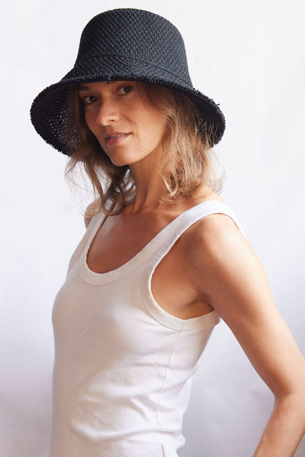 Woman wearing a black woven bucket hat and white tank top against a white background