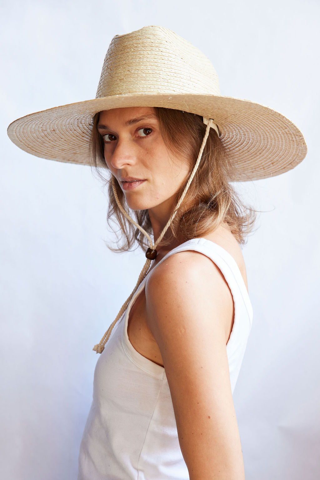 Woman wearing a wide-brimmed straw hat against a light background
