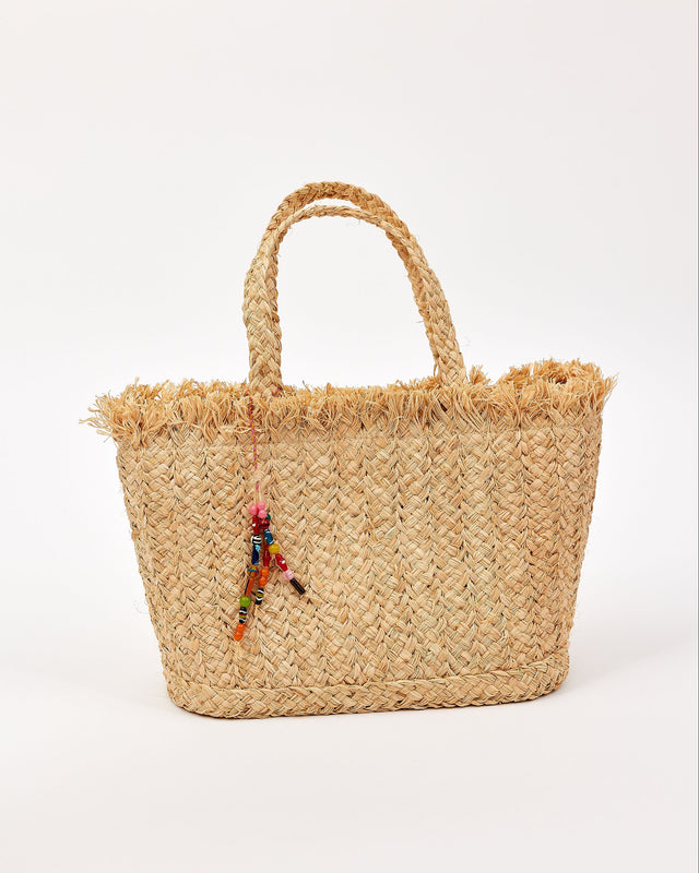 Woven straw bag with colorful charm on a white background