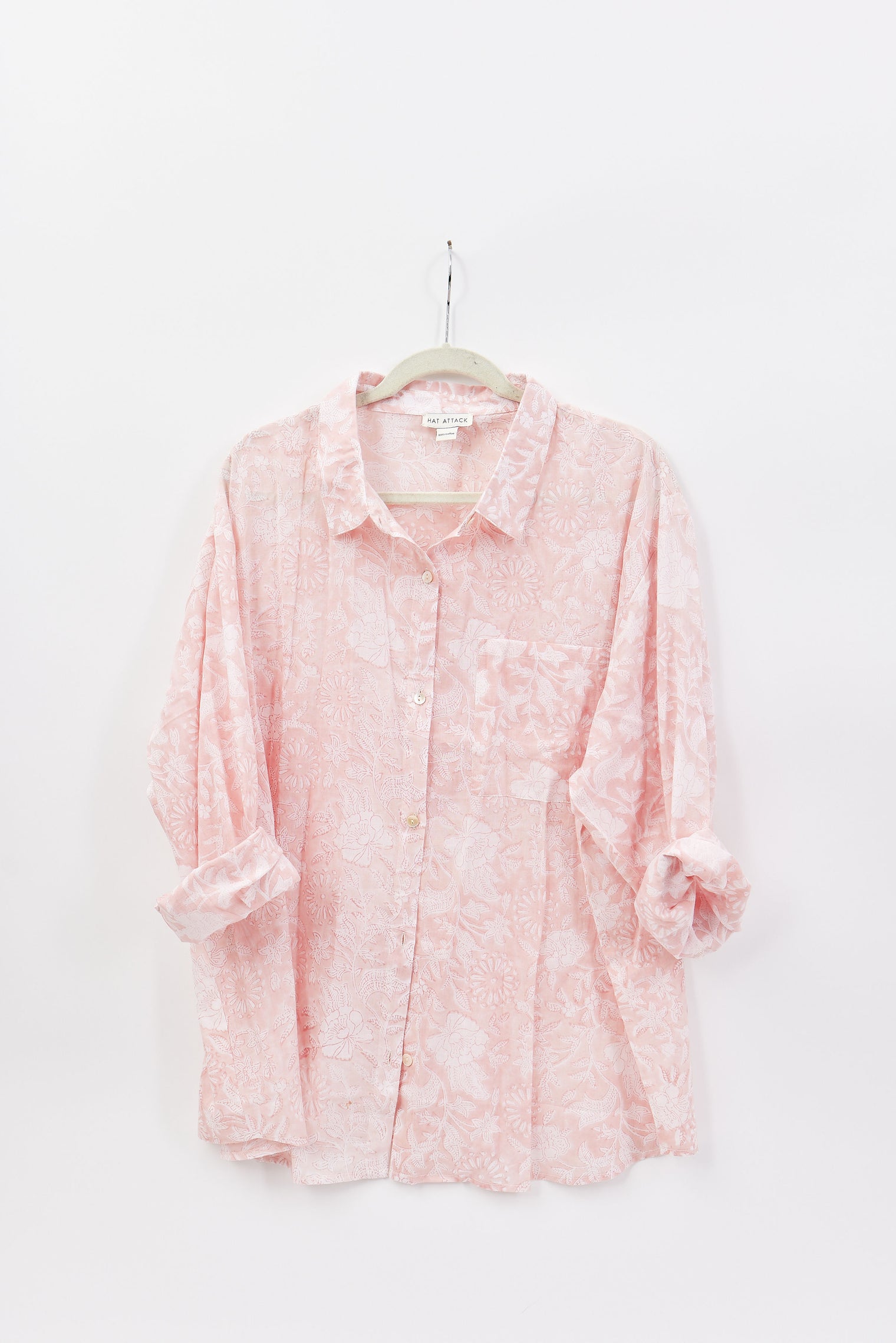 Pink floral blouse on a hanger against a white background