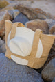 Straw bag with straps holding a sunhat on rocks