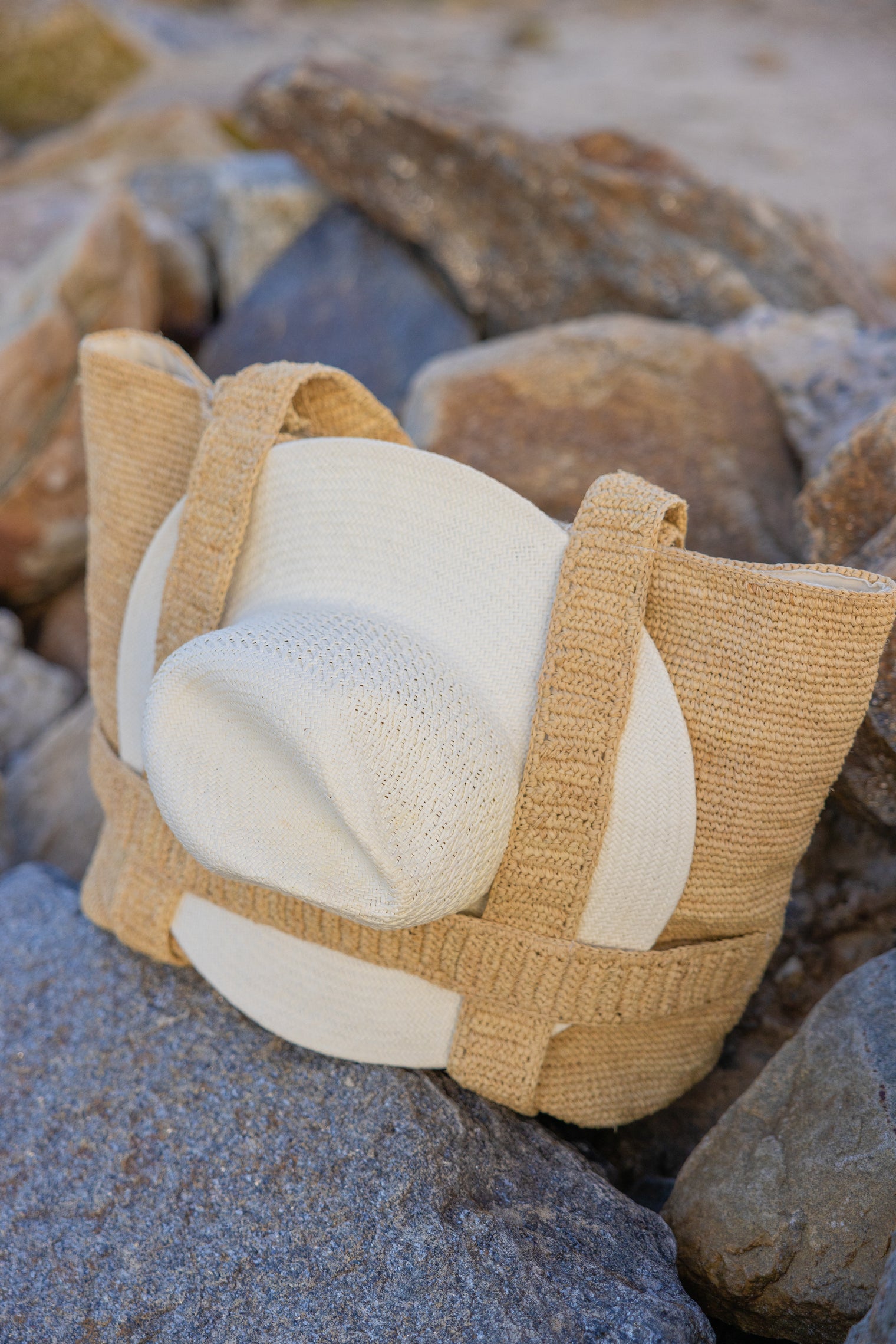 Straw bag with straps holding a sunhat on rocks