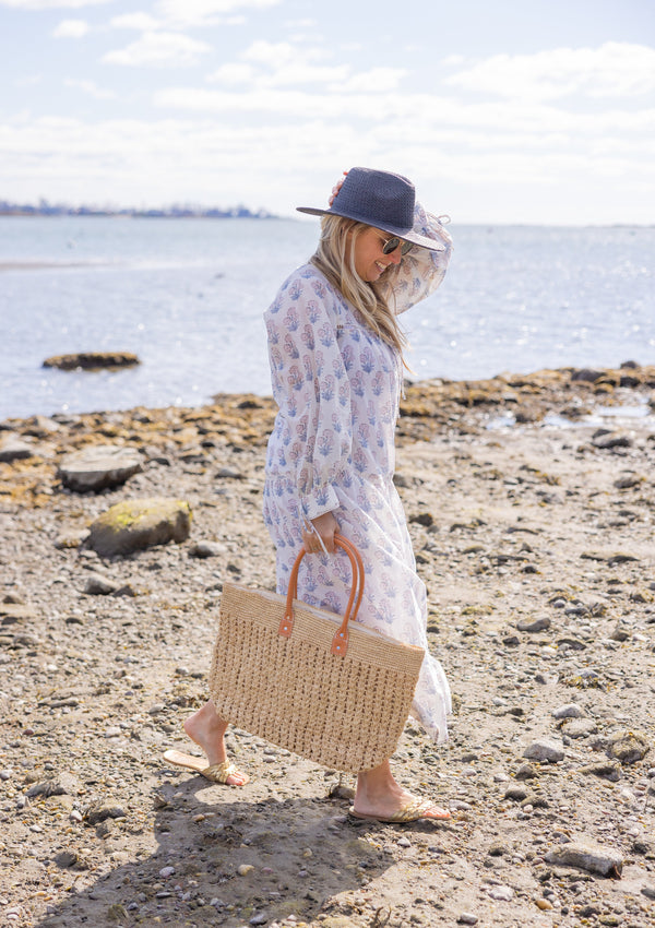 Vented Sun Hat in black on model walking on the beach with a straw beach bag