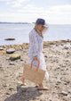 Vented Sun Hat in black on model walking on the beach with a straw beach bag
