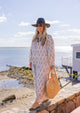 Vented Sun Hat in black on model walking on the beach with a straw beach bag and sunglasses