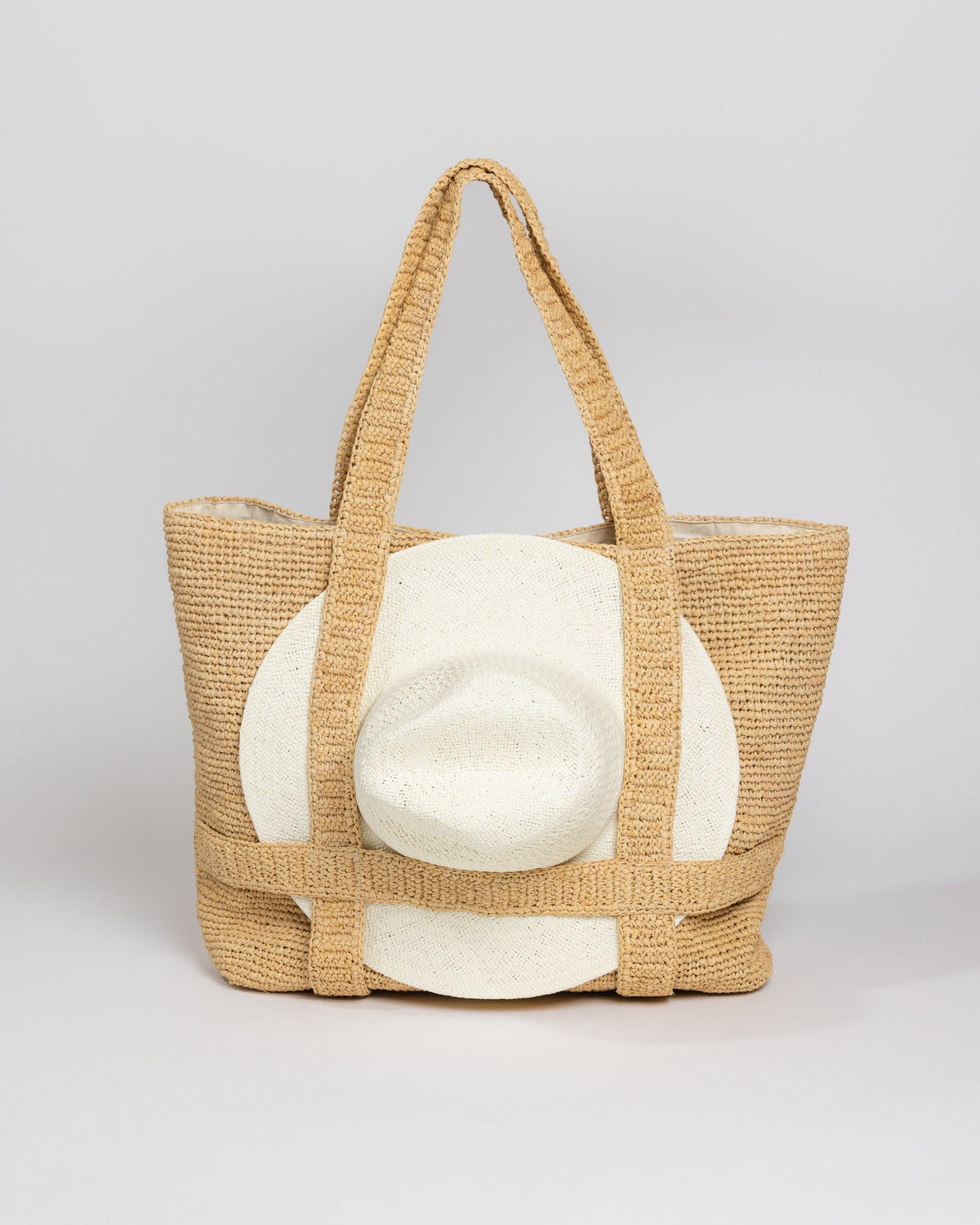 Straw bag with straps holding a sun hat with handle drop standing up