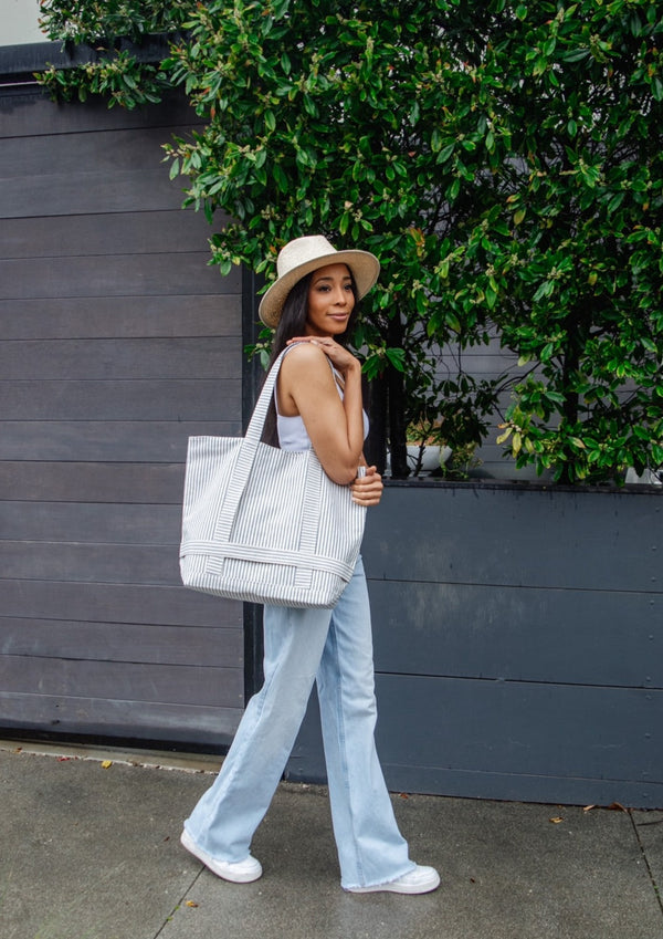 Model walking outside and holding a blue and white striped tote bag over her shoulder