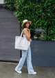 Model walking outside and holding a blue and white striped tote bag over her shoulder