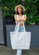 Model standing outside wearing a sun hat and holding a blue and white striped tote bag