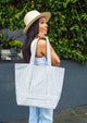 Model wearing a sun hat and holding a blue and white striped tote bag