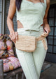 Model wearing straw belt bag and light green outfit