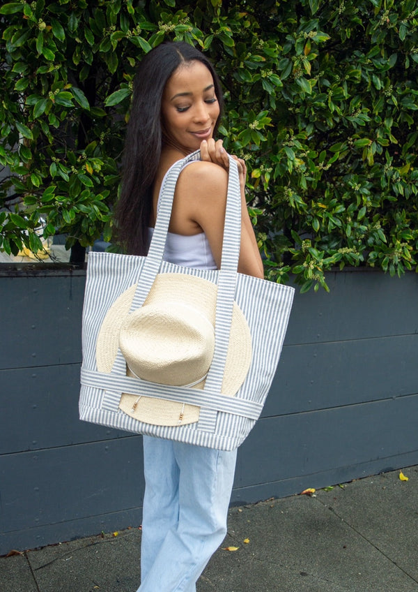 Model looking down at blue and white striped tote bag with sun hat attached