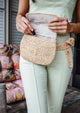Model wearing straw belt bag and putting lip gloss inside