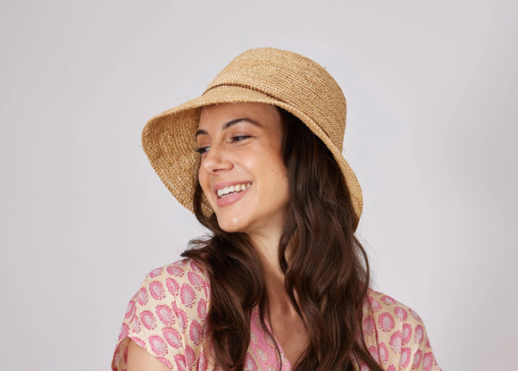 Smiling woman in a straw hat and pink dress enjoys a sunny day.