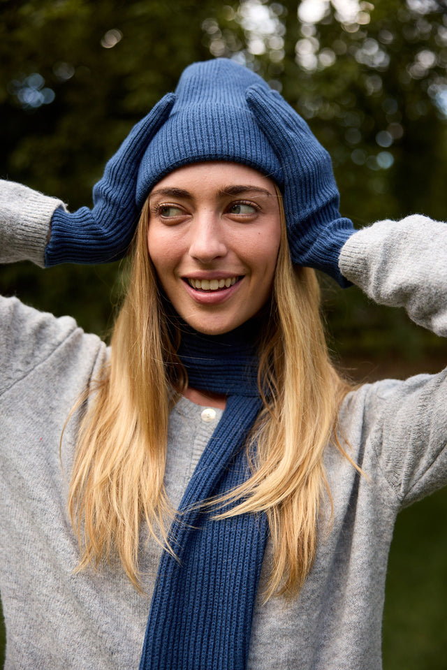 Woman with long blonde hair wearing a navy ribbed beanie, matching navy knit scarf and gloves, and a gray sweater
