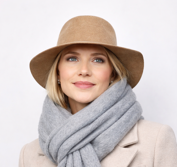 Woman wearing a beige coat, brown hat, and gray scarf against a white background