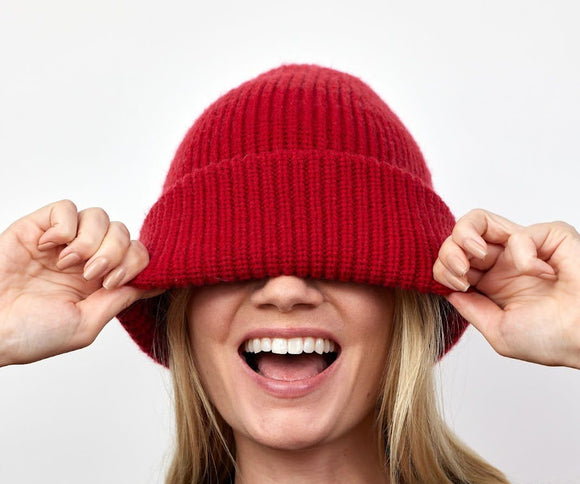 Woman covering head and eyes with red beanie.