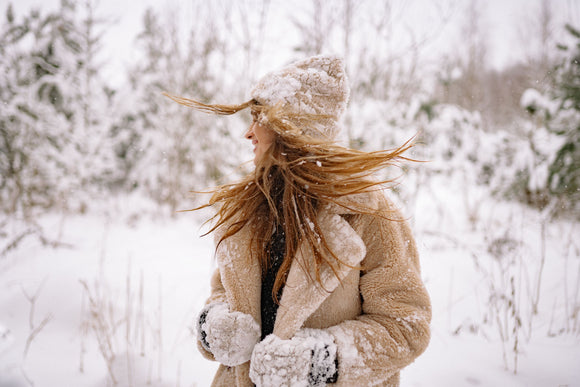 A woman in a snowy landscape wearing a hat and gloves, shielding her face from the winter sun.