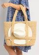 Model holding straw tote bag with white sun hat attached