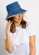 Model wearing denim fringed bucket hat with brown trim