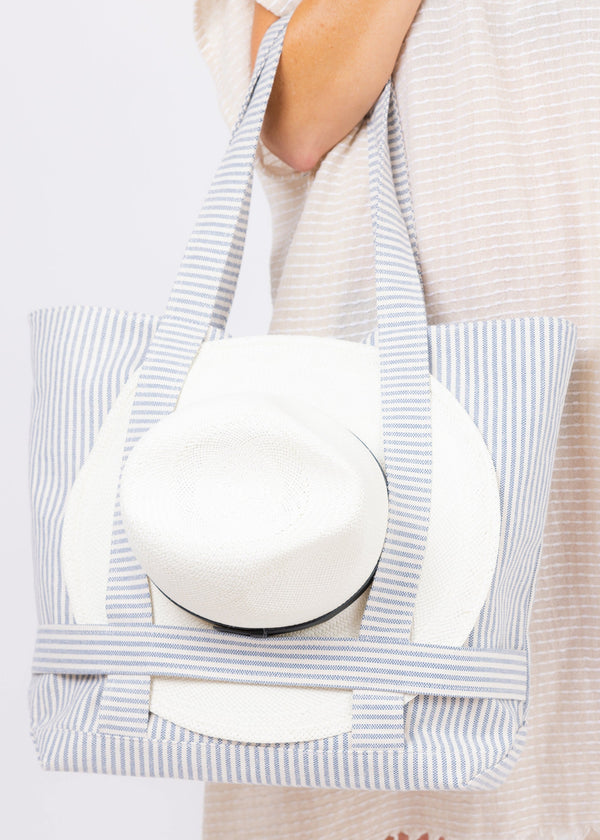 Model holding blue and white striped canvas bag with hat attached 