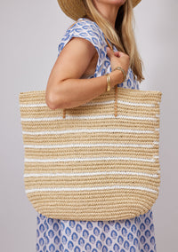 Model holding straw tote with white stripes over her shoulder