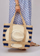 Model holding a navy stripe tote bag with a sun hat attached 