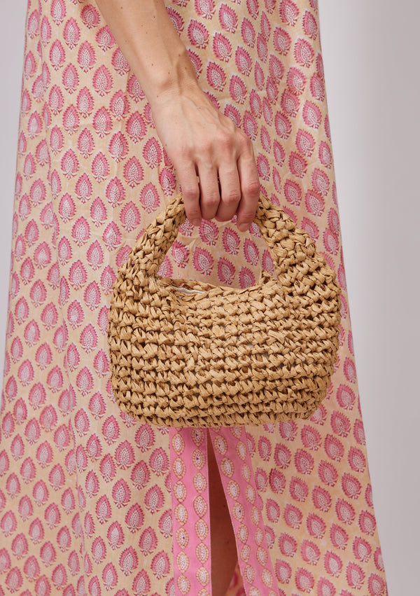 Model holding tan small slouch bag and wearing pink kaftan