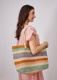 Model wearing pink kaftan and multi striped tote on shoulder