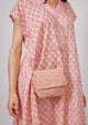 Small pink straw crossbody bag on model wearing pink kaftan