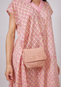 Small pink straw crossbody bag on model wearing pink kaftan