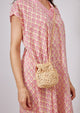 Model wearing small straw pouchette and pink kaftan