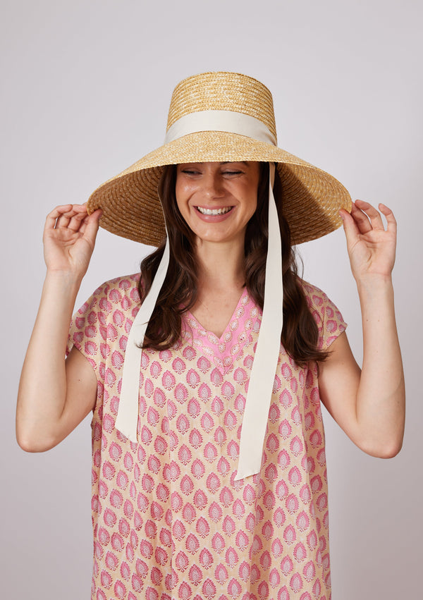 Large straw sun hat with ivory ribbon tie on model holding hat brim