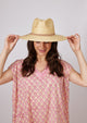 Model wearing straw brimmed hat with tan leather detail and holding brim