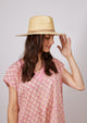 Model wearing pink kaftan and straw hat with tan leather detail