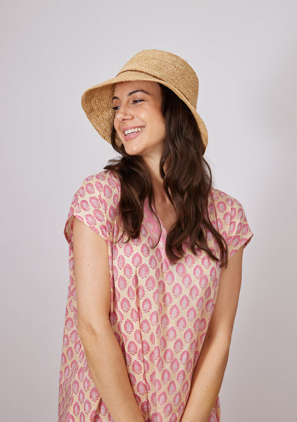Model smiling while wearing a straw bucket hat with brown stripe