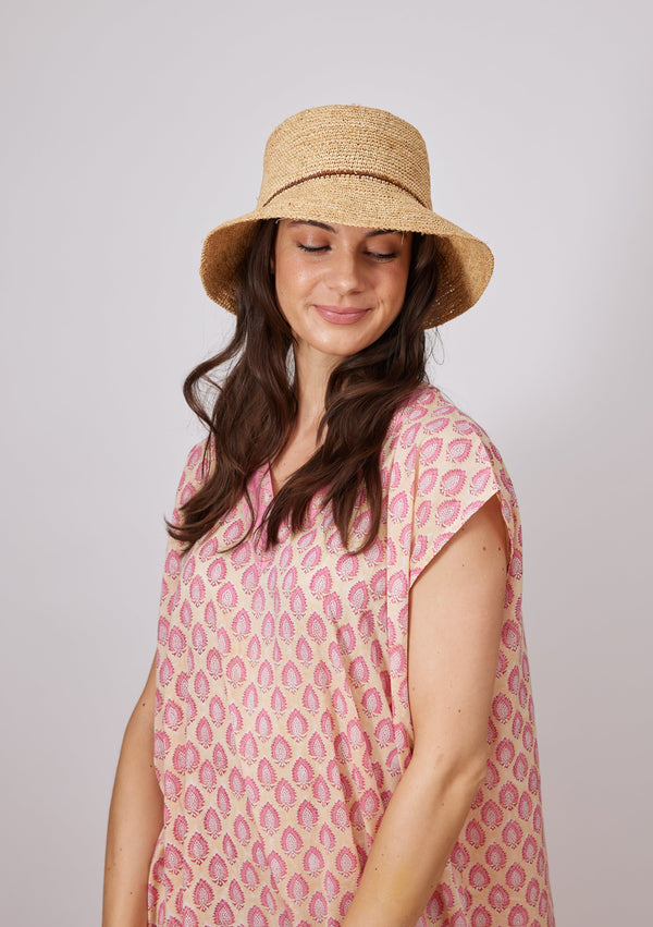 Model looking down wearing a straw bucket hat with a brown trim
