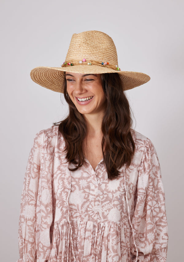 Model laughing while wearing straw hat with colorful bead trim