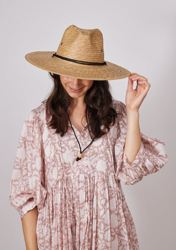 Model holding brim of straw sun hat with black trim and chinstrap