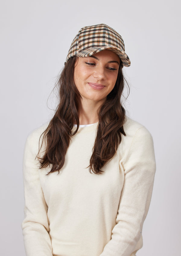 Model looking down and wearing an ivory and brown small plaid baseball cap