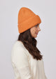 Model wearing orange knit cuffed beanie while looking to her left
