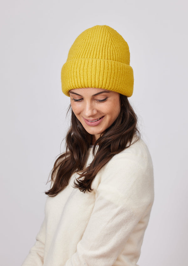 Yellow knit beanie in ivory sweater looking down